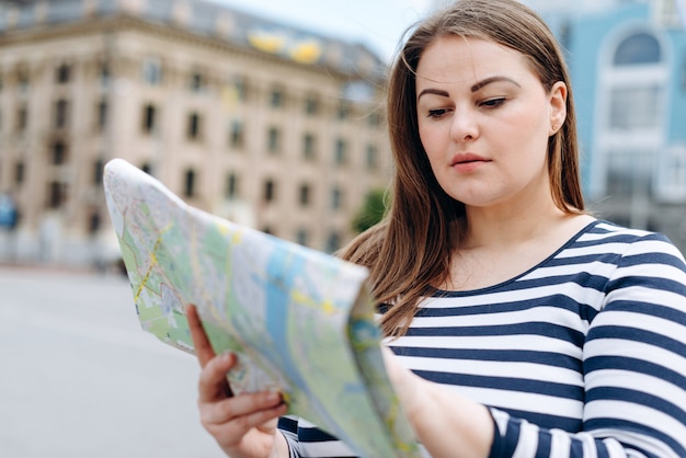 Foto mulher jovem turista fica na praça, estudando cuidadosamente o mapa turístico