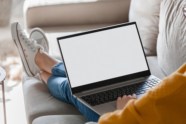 Mulher jovem usando a tela do laptop em branco, deitada no sofá em casa