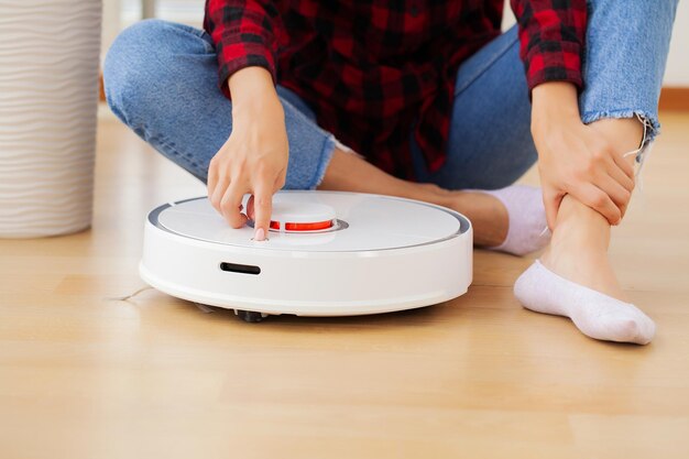 Mulher jovem usando aspirador de pó automático para limpar o chão, controlando o robô de trabalho doméstico da máquina.