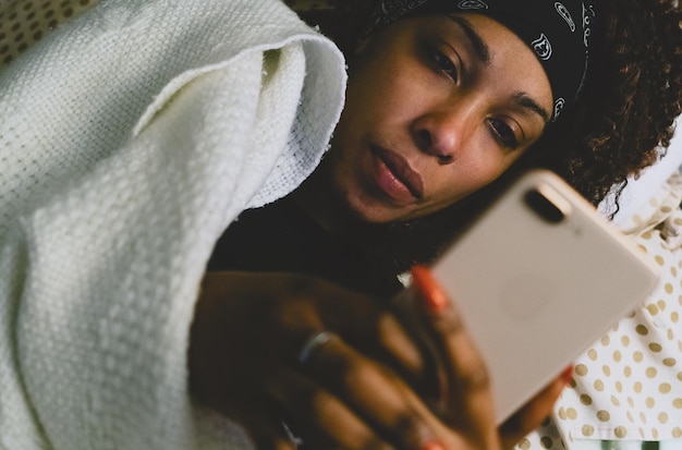 Mulher jovem usando celular enquanto está deitada na cama em casa