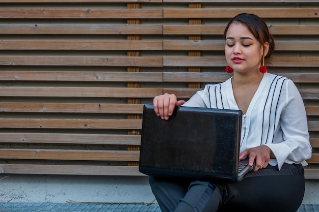 Foto mulher jovem usando laptop enquanto está sentada na calçada