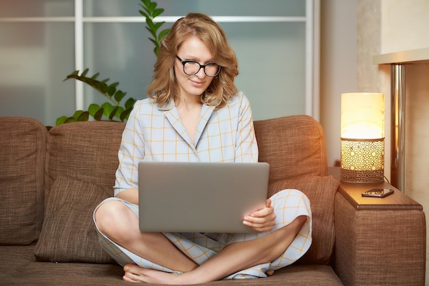 Mulher jovem usando laptop enquanto está sentada no sofá em casa