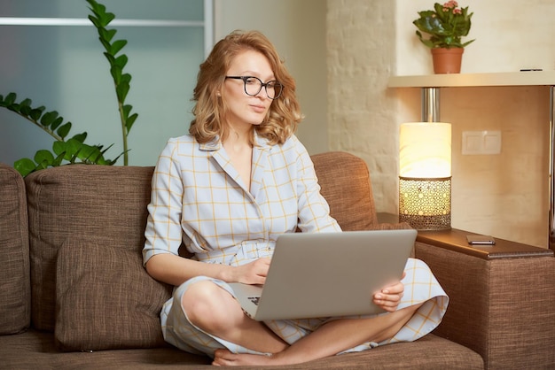 Mulher jovem usando laptop enquanto está sentada no sofá em casa