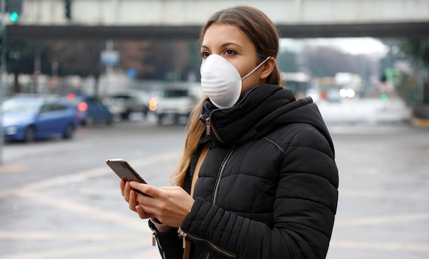 Mulher jovem usando máscara facial usando aplicativo de telefone inteligente na cidade