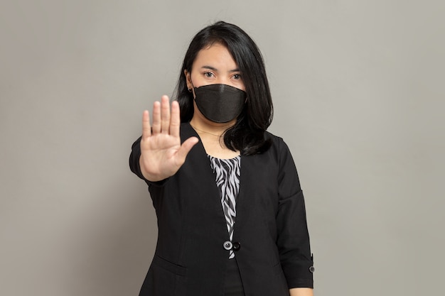 Mulher jovem usando máscara preta com um gesto de parada
