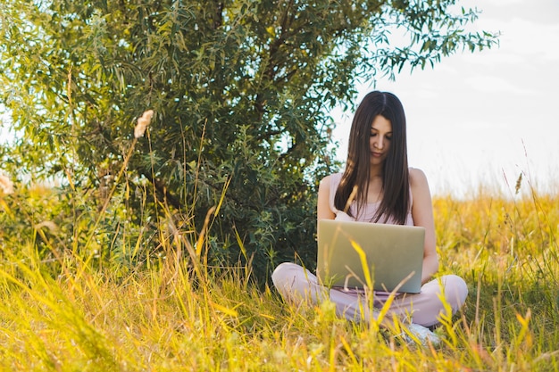 Mulher jovem usando o laptop no campo