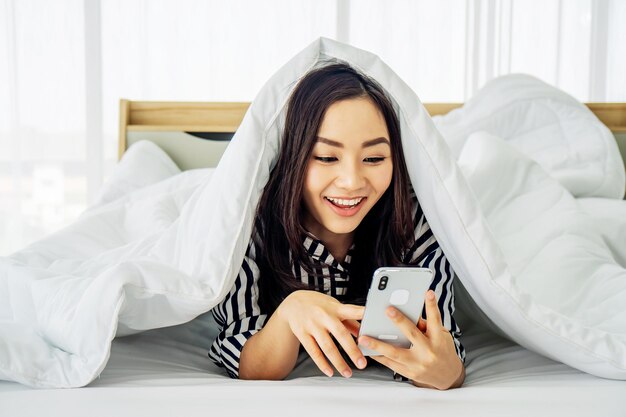Mulher jovem usando o telefone enquanto se relaxa na cama em casa