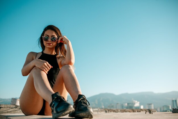 Mulher jovem usando óculos de sol sentada na montanha contra o céu
