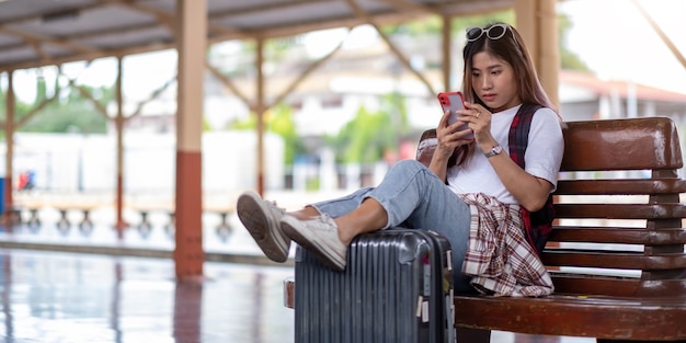 Mulher jovem usando seu smartphone enquanto espera o trem na estação de trem.