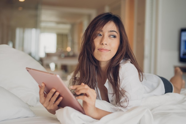 Mulher jovem usando tablet digital enquanto está deitada na cama em casa