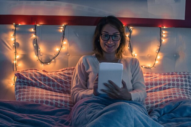 Foto mulher jovem usando tablet digital enquanto está sentada na cama em casa