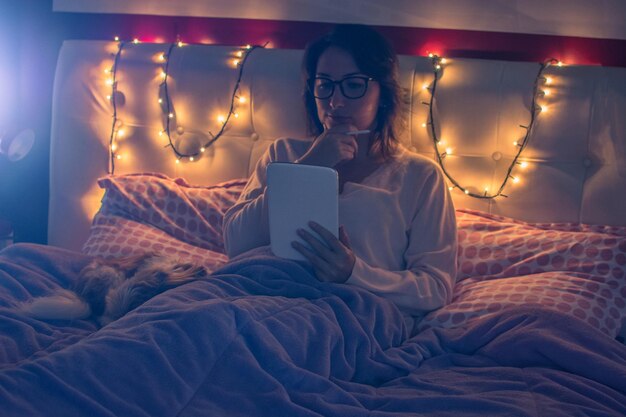 Foto mulher jovem usando tablet digital enquanto está sentada na cama em casa