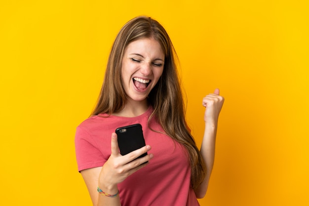 Foto mulher jovem usando telefone celular isolado em amarelo comemorando uma vitória