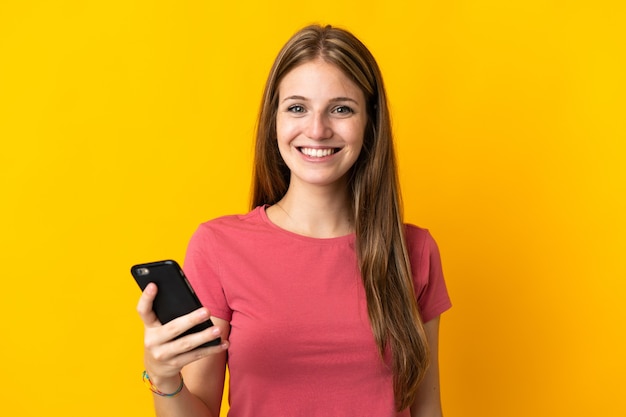 Mulher jovem usando telefone celular isolado em amarelo sorrindo muito