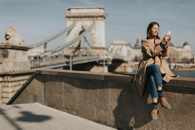 Mulher jovem, usando, telefone móvel, com, ponte chain, em, fundo, em, budapest