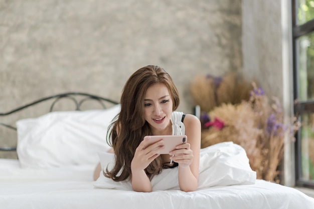 Mulher jovem usando telefone móvel enquanto deitada na cama em casa