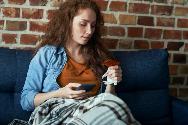 Foto mulher jovem usando telefone móvel enquanto está sentada no sofá em casa