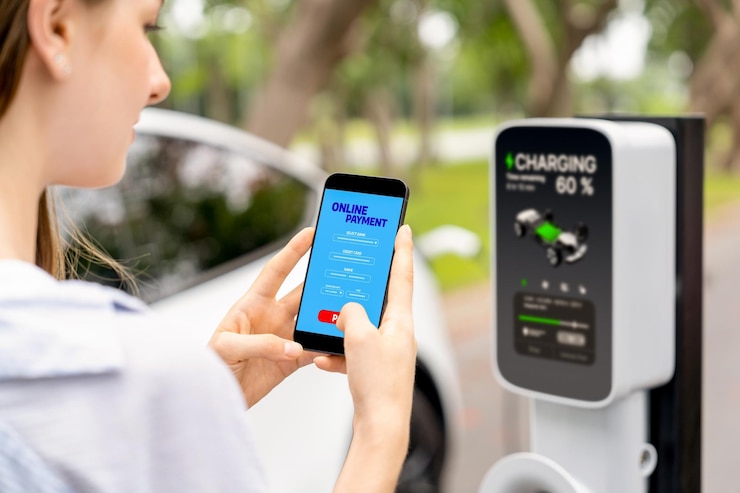 Foto mulher jovem usando um aplicativo bancário on-line de smartphone para pagar o carregamento da bateria de um carro elétrico a partir de uma estação de carregamento de veículos elétricos durante uma viagem de férias em um parque nacional ou floresta de verão exalt