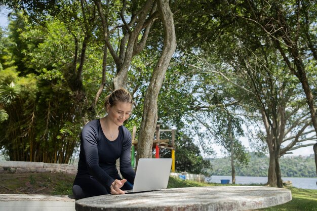 Foto mulher jovem usando um laptop durante o dia em um parque verde tecnologia de telefone móvel