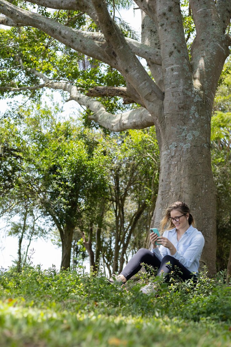 Foto mulher jovem usando um smartphone durante o dia com um parque verde ao fundo foto de alta qualidade tecnologia de telefonia móvel conceito urbano foto de elevada qualidade