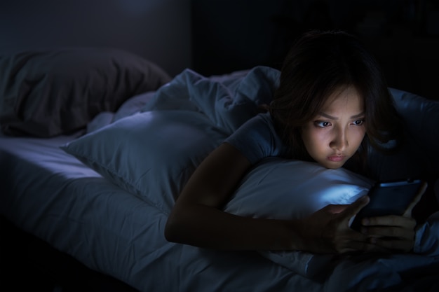 Mulher jovem usando um smartphone na cama à noite