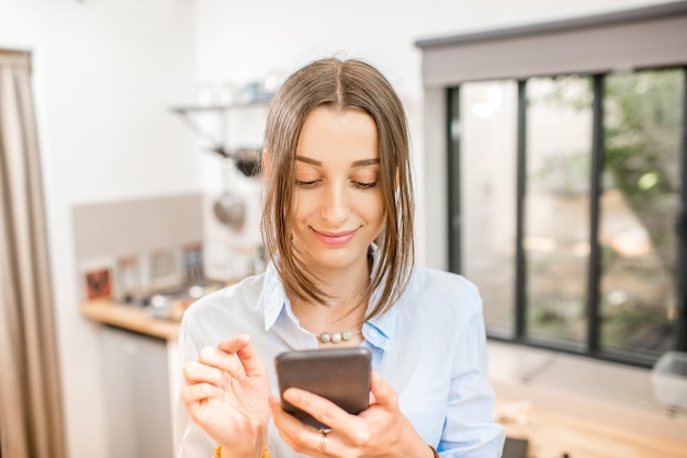 Mulher jovem usando um smartphone na cozinha