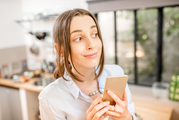 Mulher jovem usando um smartphone na cozinha