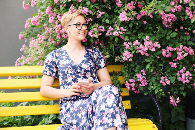 Mulher jovem usando um smartphone perto de um arbusto de flores