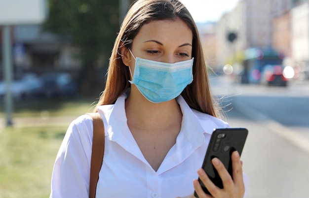 Mulher jovem usando uma máscara usando um telefone celular na rua