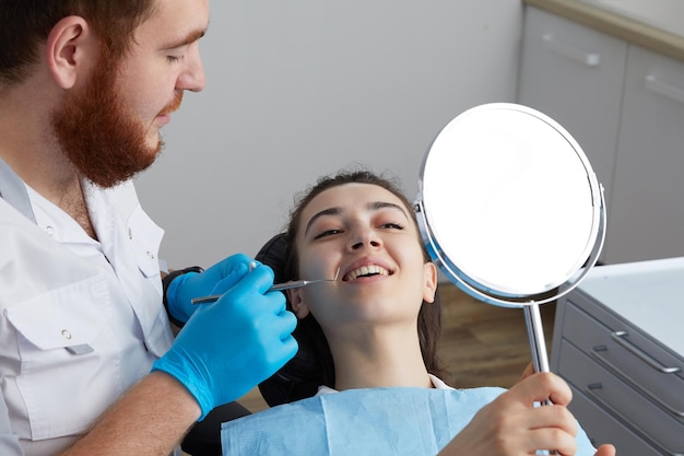 Mulher jovem verificando seu lindo sorriso no espelho após tratamento estomatológico