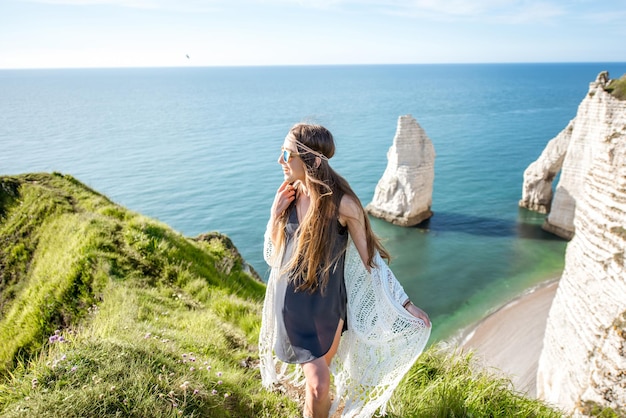 Mulher jovem vestida em estilo hippie, curtindo a natureza na costa rochosa com uma bela vista para o oceano na França