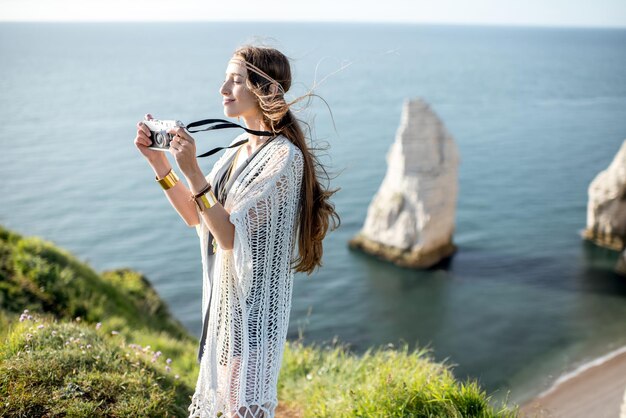 Mulher jovem vestida em estilo hippie fotografando uma bela paisagem na costa rochosa da França