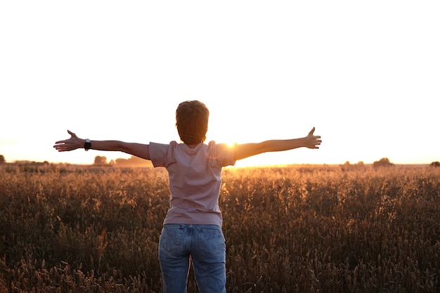 Mulher jovem vestindo jeans e camisa rosa congratula-se com o pôr do sol da noite de verão.