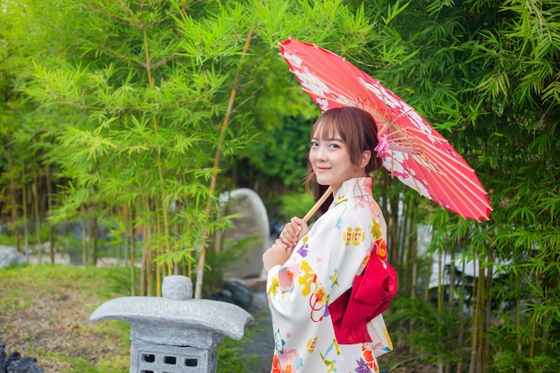 Mulher jovem vestindo kimono ou yukata tradicional japonês segurando um guarda-chuva em um parque com árvores de bambu