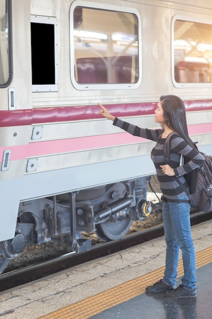 Mulher jovem viajante com mochila, verificando o destino do quadro branco de computador em branco antes de entrar no trem