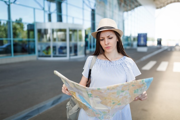 Mulher jovem viajante insatisfeita segurando um mapa de papel, em pé no aeroporto internacional