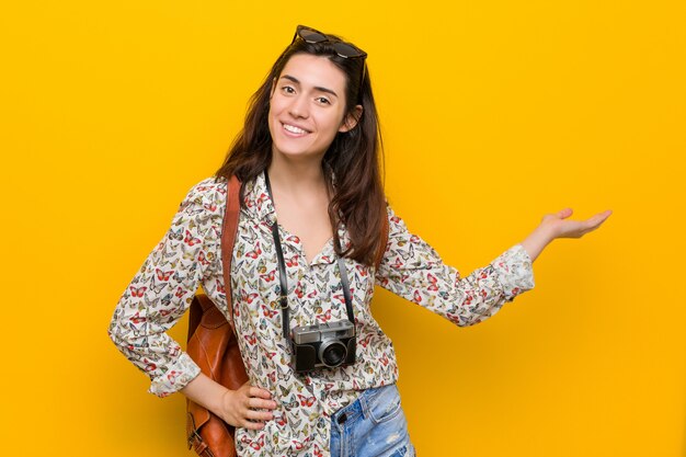 Mulher jovem viajante morena mostrando um espaço de cópia na palma da mão e segurando a outra mão na cintura.