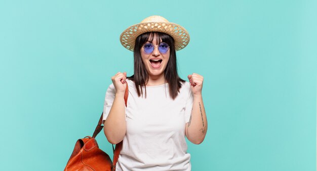 Mulher jovem viajante sentindo-se chocada, animada e feliz, rindo e comemorando o sucesso, dizendo uau!