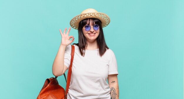 Mulher jovem viajante sentindo-se feliz, relaxada e satisfeita, mostrando aprovação com gesto de ok, sorrindo