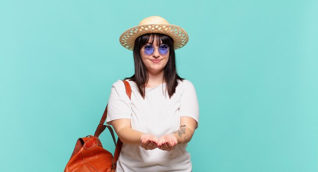 Mulher jovem viajante sorrindo feliz com um olhar amigável, confiante e positivo, oferecendo e mostrando um objeto ou conceito