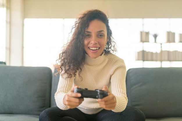 Mulher Laitin jogando videogame com as mãos segurando um joystick no sofá em casa