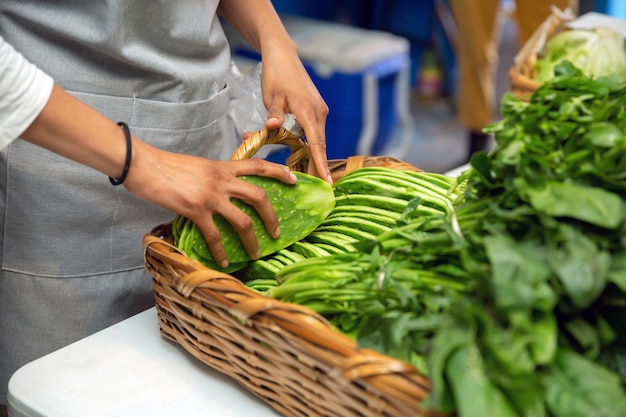 Mulher latina colocando nopales em uma cesta com outros vegetais verdes para vender