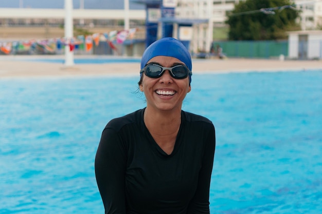 Mulher latina com boné e óculos de pé em uma piscina ao ar livre