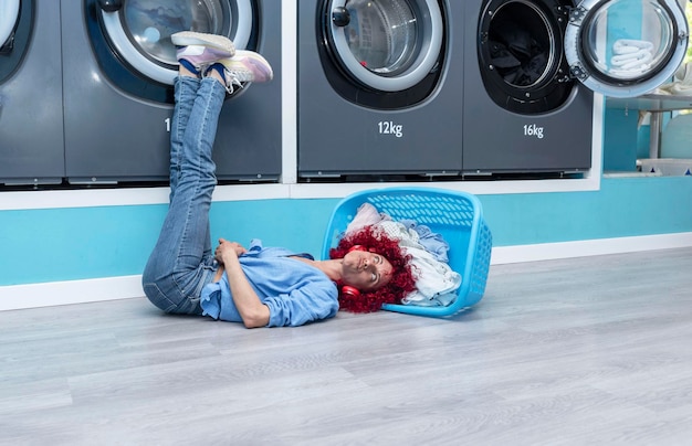 Mulher latina com cabelo afro vermelho deitada no chão na cesta em uma lavanderia automática azul