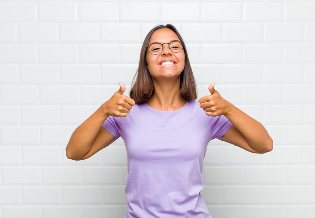 Mulher latina com um sorriso largo, parecendo feliz, positiva, confiante e bem-sucedida, com os dois polegares para cima