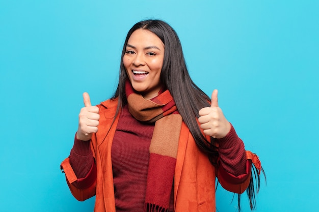 Mulher latina com um sorriso largo, parecendo feliz, positiva, confiante e bem-sucedida, com os dois polegares para cima