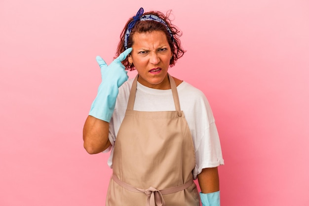 Mulher latina de meia-idade isolada em fundo rosa, mostrando um gesto de decepção com o dedo indicador.