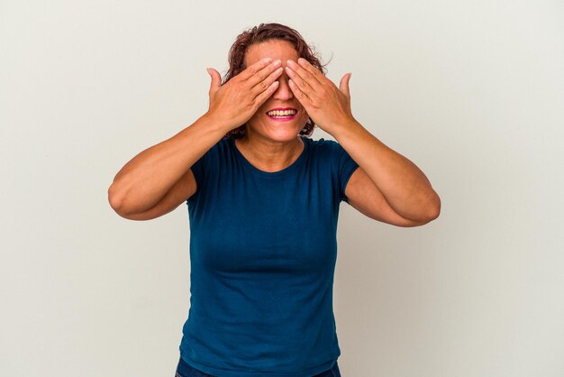 Mulher latina de meia-idade isolada no fundo branco com medo de cobrir os olhos com as mãos.