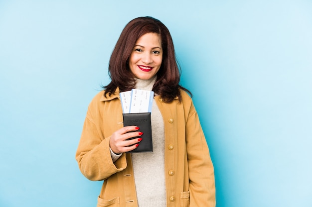 Mulher latina de meia idade segurando um passaporte isolado feliz, sorridente e alegre.