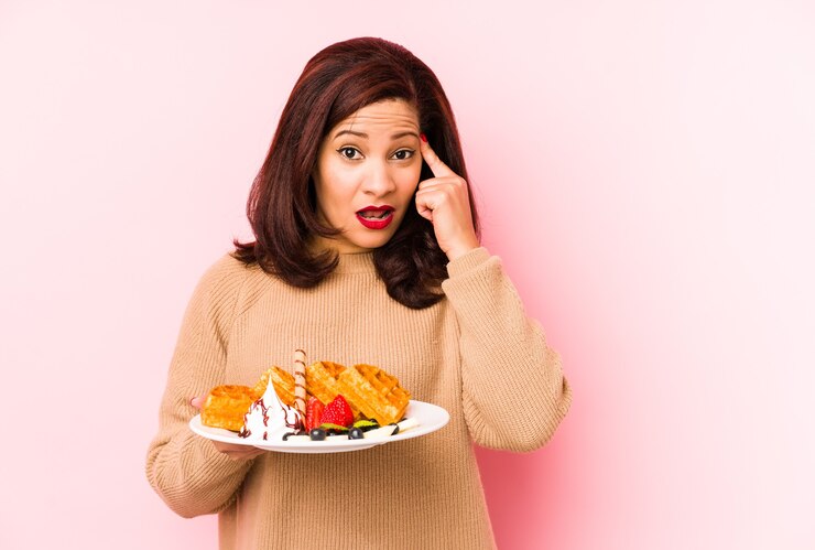 Foto mulher latina de meia-idade segurando um waffle isolado, mostrando um gesto de decepção com o dedo indicador.